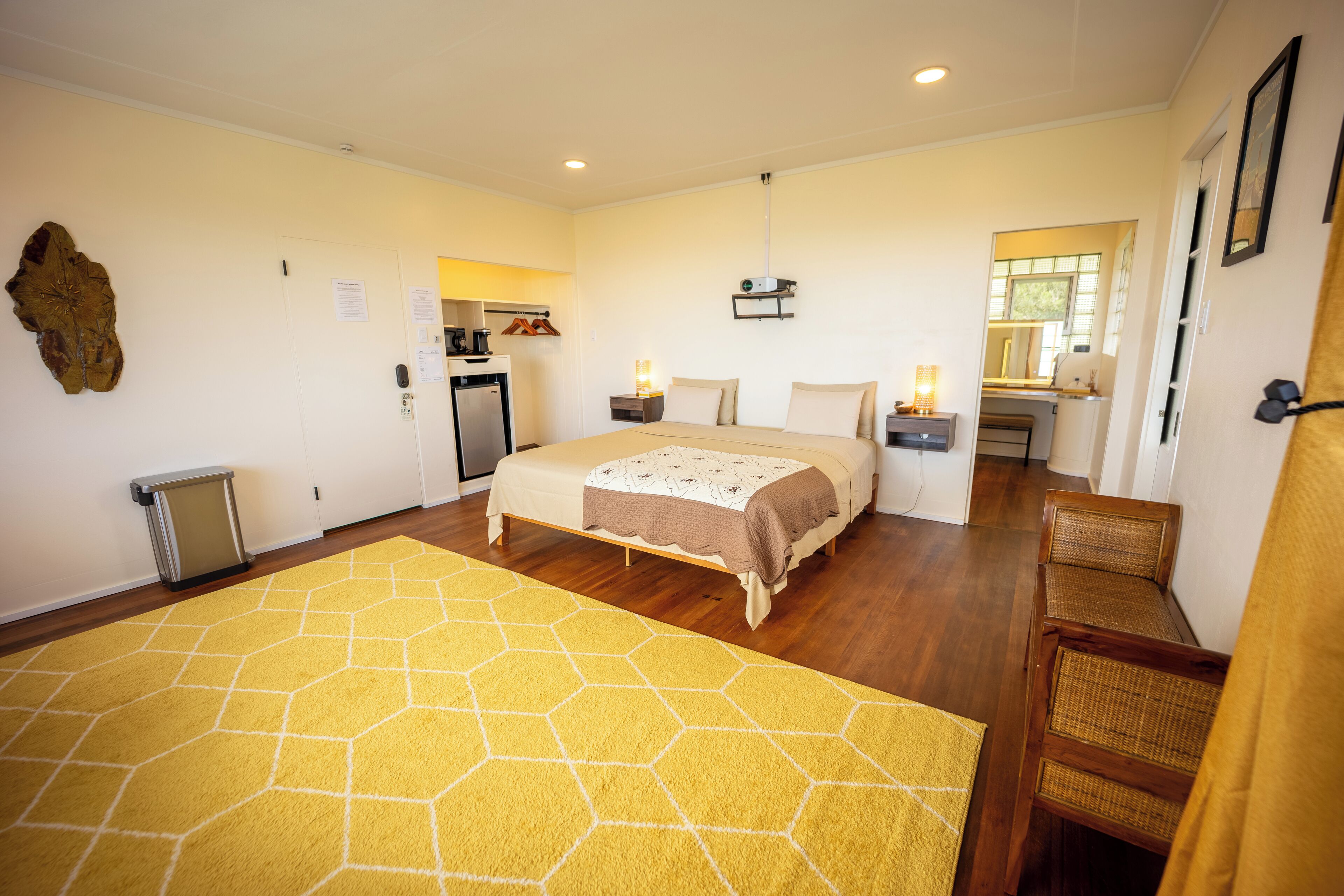 A hotel room with a large bed, a small kitchenette, a bathroom, and a yellow rug.