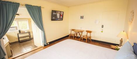 Une chambre d’hôtel avec un grand lit, un bureau avec deux chaises, une petite table, un téléviseur fixé au mur et une porte avec un interrupteur.
