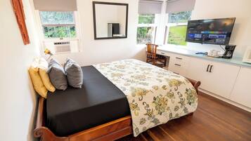 Un dormitorio con cama, escritorio, silla, televisor y ventana con vistas a zonas verdes.