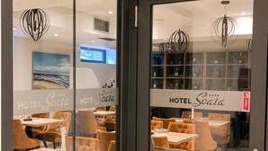 A modern hotel interior with glass doors, a dining area with tables and chairs, and a visible bar area with shelves of bottles. - Hotel Scala dOro (Vodice)