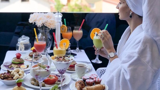 A person seated at a table with a variety of breakfast items and drinks, overlooking a cityscape with red-roofed buildings. - Hotel Scala dOro (Vodice)