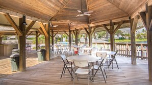 An outdoor wooden deck with tables and chairs, a ceiling fan, and a view of a lake and houses in the background. - 1900 ft from beach Luxury Jupiter Beach Villa! private entrance community pool (Jupiter)