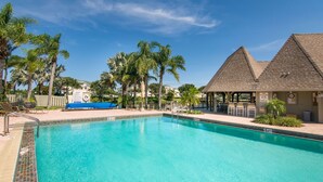 A clear blue pool with a tiled edge, surrounded by palm trees and a covered seating area. - 1900 ft from beach Luxury Jupiter Beach Villa! private entrance community pool (Jupiter)