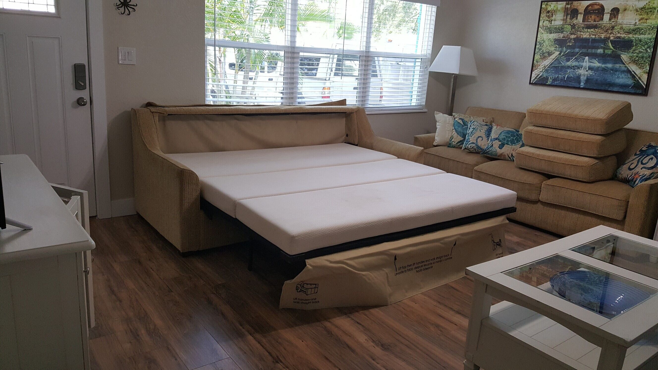 Ein kleines Zimmer mit Schlafsofa, Tisch und Fenster mit Jalousien.