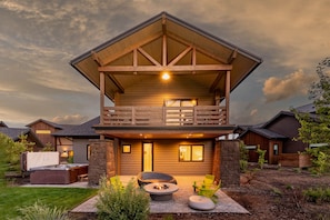 A two-story log cabin with a balcony, outdoor seating, and a fire pit.