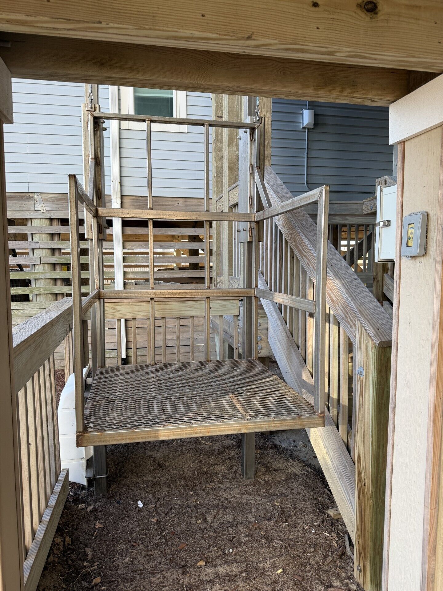 A wooden outdoor enclosure with a metal grid floor, surrounded by wooden railings and a metal gate.