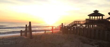 A beach with a wooden walkway leading to a gazebo-like structure.