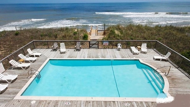A pool with a view of the ocean, surrounded by lounge chairs and a wooden deck. - 2 Bed, 2 Bath Condo with an Oceanfront Pool and Ocean View from the Unit. (Kill Devil Hills)