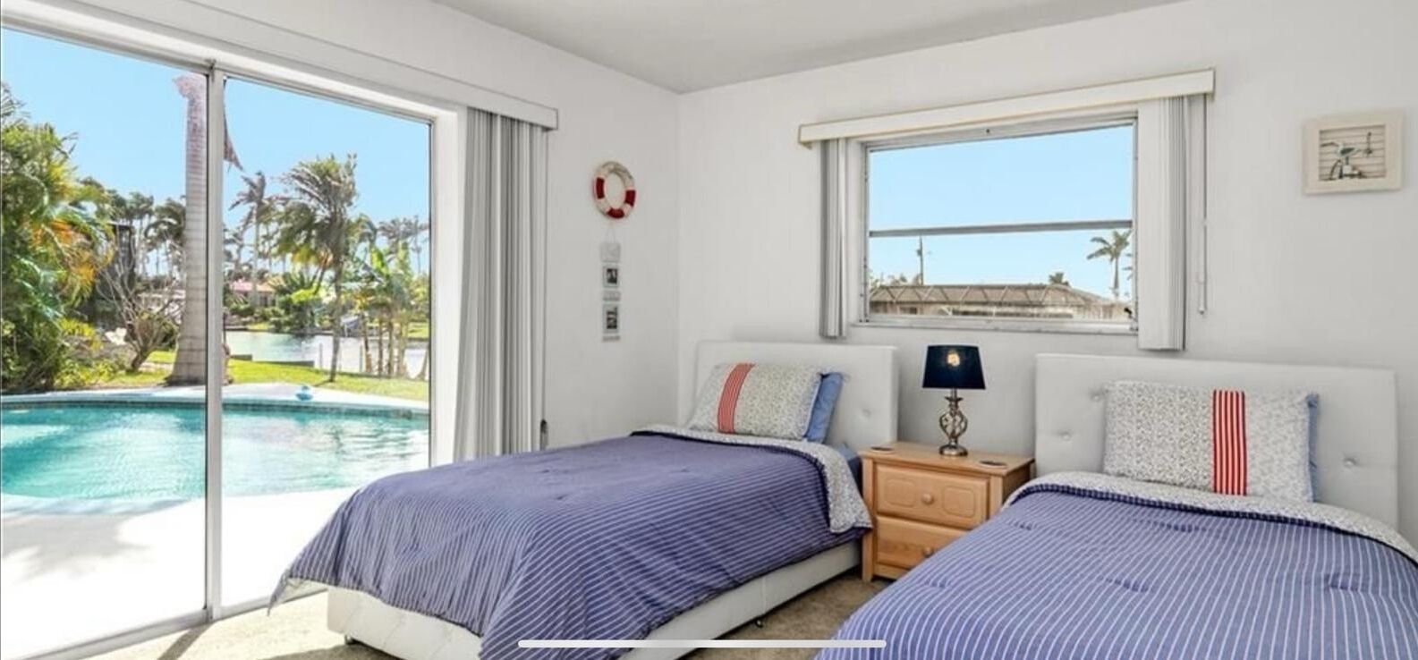 A bedroom with two beds, a window, and a view of a swimming pool.