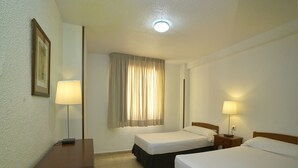 Ett hotellrum med två sängar, ett skrivbord, en lampa, ett fönster med gardiner och en taklampa.