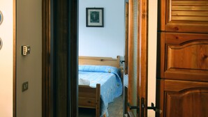 Ein Flur mit einer Holztür, einem Bett mit blauer Bettdecke und einer Blumenkomposition auf einem Tisch.