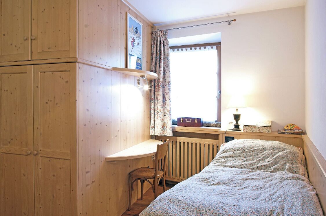 Een slaapkamer met een houten garderobe, een bureau, een stoel, een radiator en een bed.