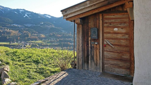 Un bâtiment en bois doté d’une porte et offrant une vue sur une vallée et des montagnes.
