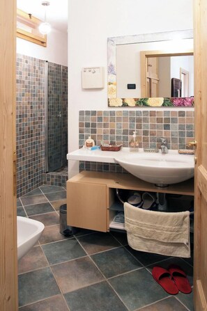 Un baño con lavamanos blanco, un espejo y zona de ducha.