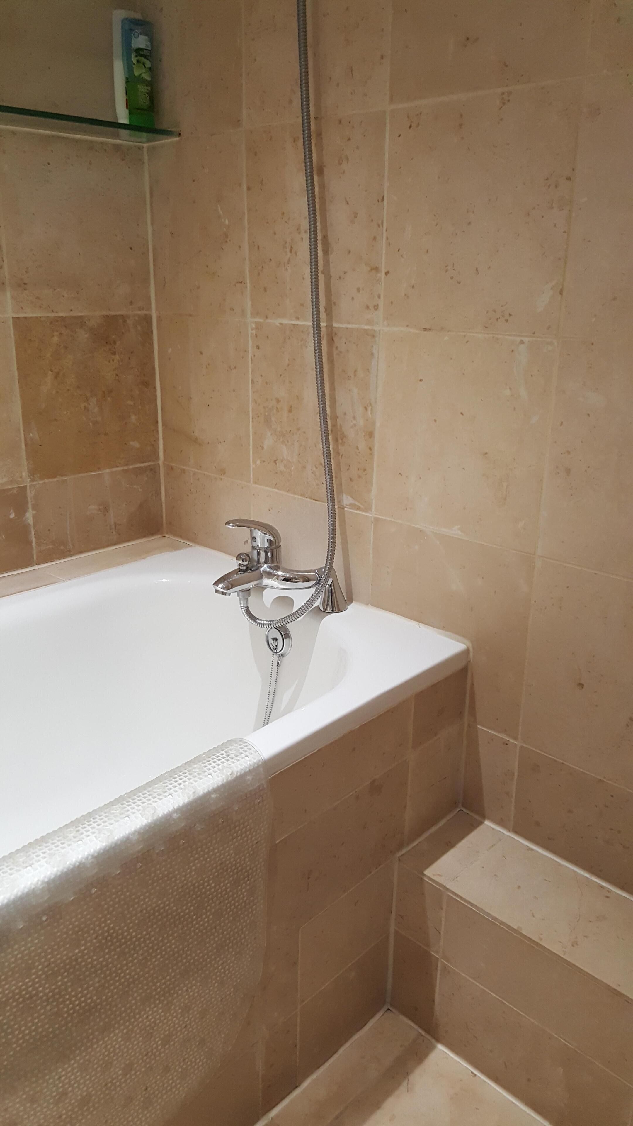 A bathroom with a bathtub, a showerhead, and beige tiles.