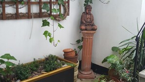 A small courtyard with a wooden trellis, a terracotta statue, and various potted plants. - Bright Garden Flat w/ Patio | 5★ Reviews | 5 min to Tube & Westfield (London)