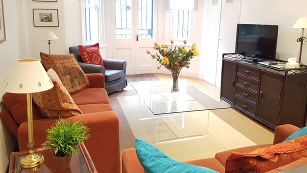 A modern living room with a sofa, a coffee table, a TV, and a cabinet. - Bright Garden Flat w/ Patio | 5★ Reviews | 5 min to Tube & Westfield (London)