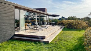 A modern house with a glass-enclosed patio, outdoor seating, and a wooden deck.