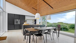 A modern kitchen with dark cabinetry, a wooden ceiling, and a large window overlooking a garden.