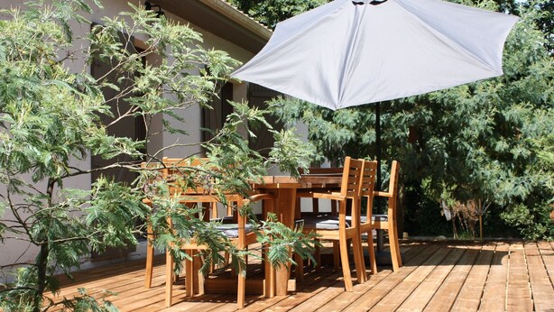 Une terrasse en bois avec une table et des chaises, entourée d’arbres.