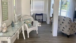 Un salón decorado con motivos playeros, que incluye muebles de mimbre, una mesa de centro de vidrio y vistas al exterior.