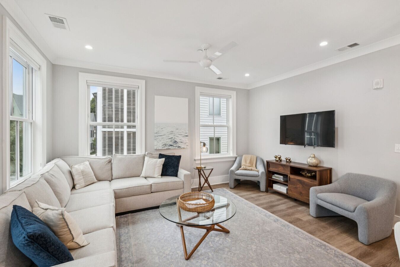 A modern living room with a sectional sofa, a glass coffee table, a grey armchair, and a television mounted on the wall.