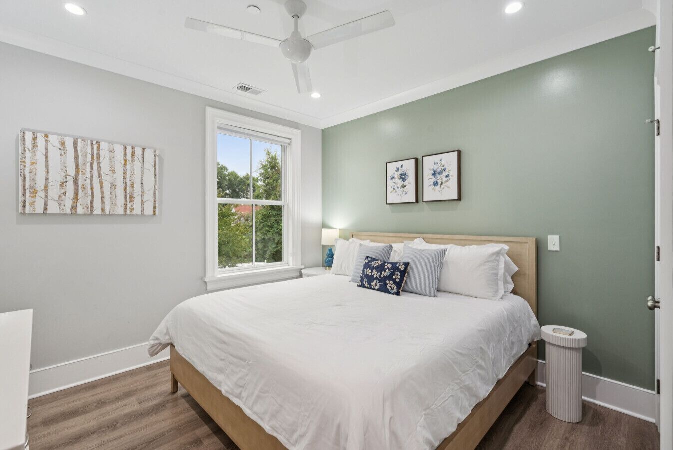 A bedroom with a large bed, a ceiling fan, a window, and two framed pictures on the wall.