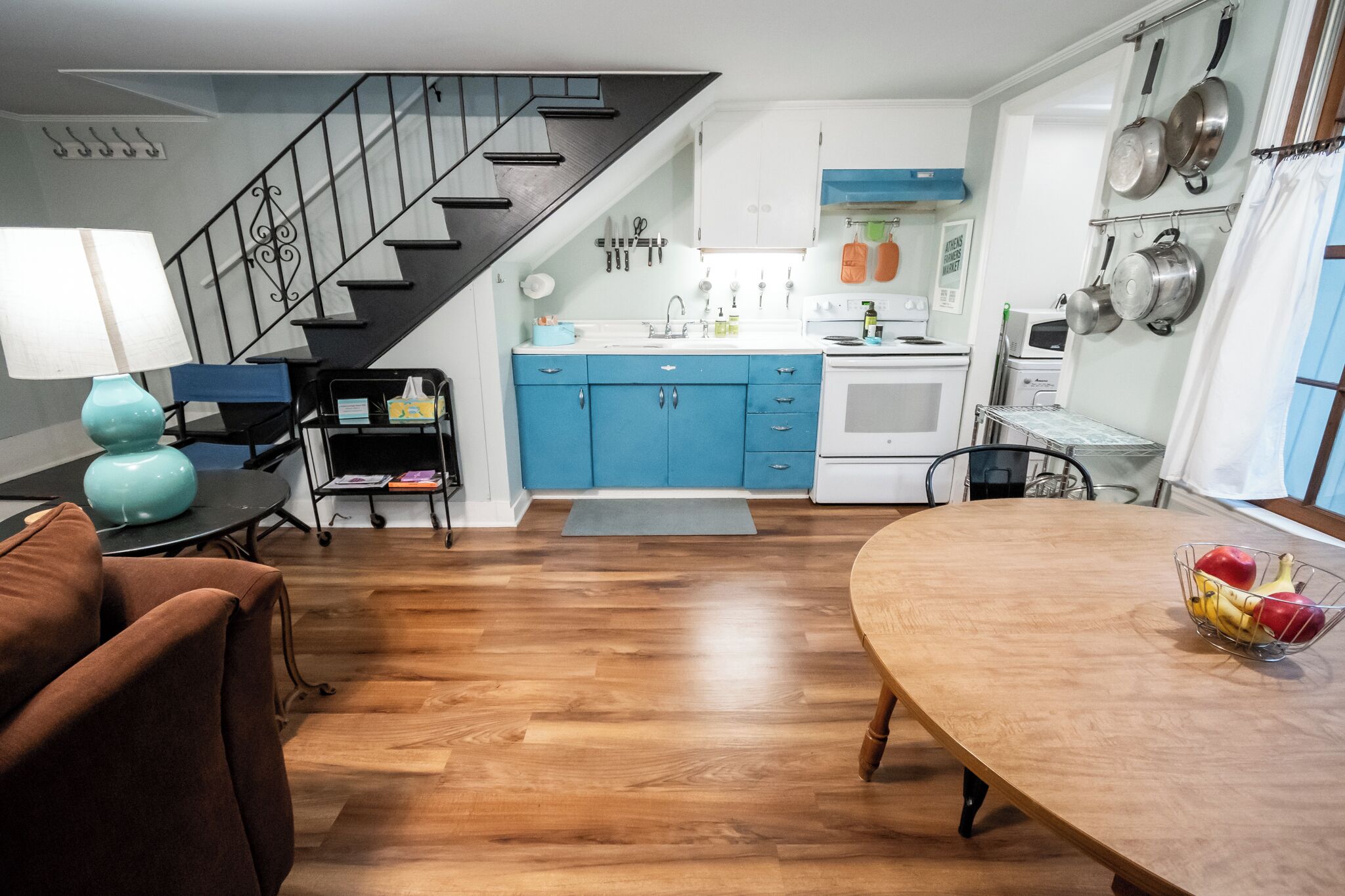 A modern kitchen with blue cabinets, a wooden dining table, and a staircase.