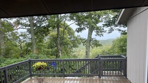 Una terraza de madera con barandilla, con vista a un área boscosa con árboles y una montaña al fondo.