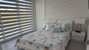 Ein Schlafzimmer mit einem Bett, einem Nachttisch, einer Lampe und einem Fenster mit Jalousien.