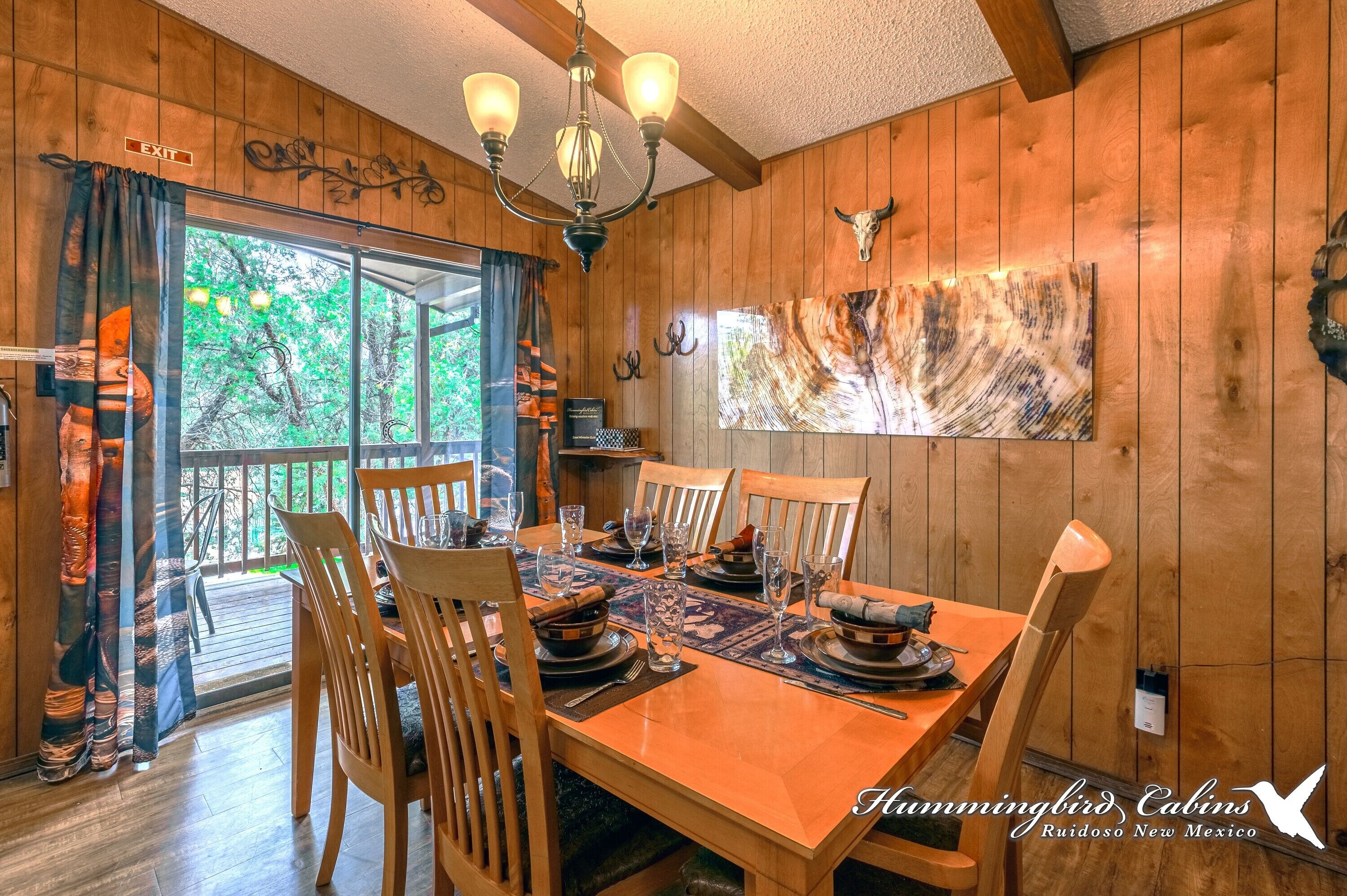 A wooden cabin interior with a dining table set for four, a chandelier, and a bull skull decoration.
