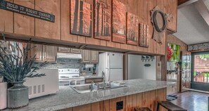A kitchen with wooden paneling, a granite countertop, stainless steel appliances, and a hanging coat rack. - Hidden Treasure | Strike Gold w/ Hot Tub Nights, Cozy Cabin Charm & Pet Friendly (Ruidoso)