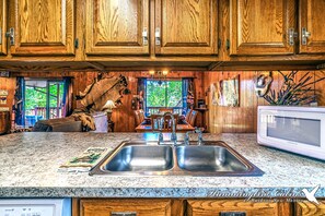 A kitchen with wooden cabinets, a granite countertop, a double sink, and a microwave. - Hidden Treasure | Strike Gold w/ Hot Tub Nights, Cozy Cabin Charm & Pet Friendly (Ruidoso)