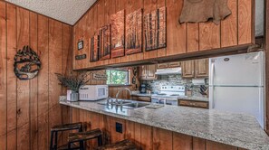 A kitchen with wooden walls, a granite countertop, a refrigerator, a stove, and a sink.