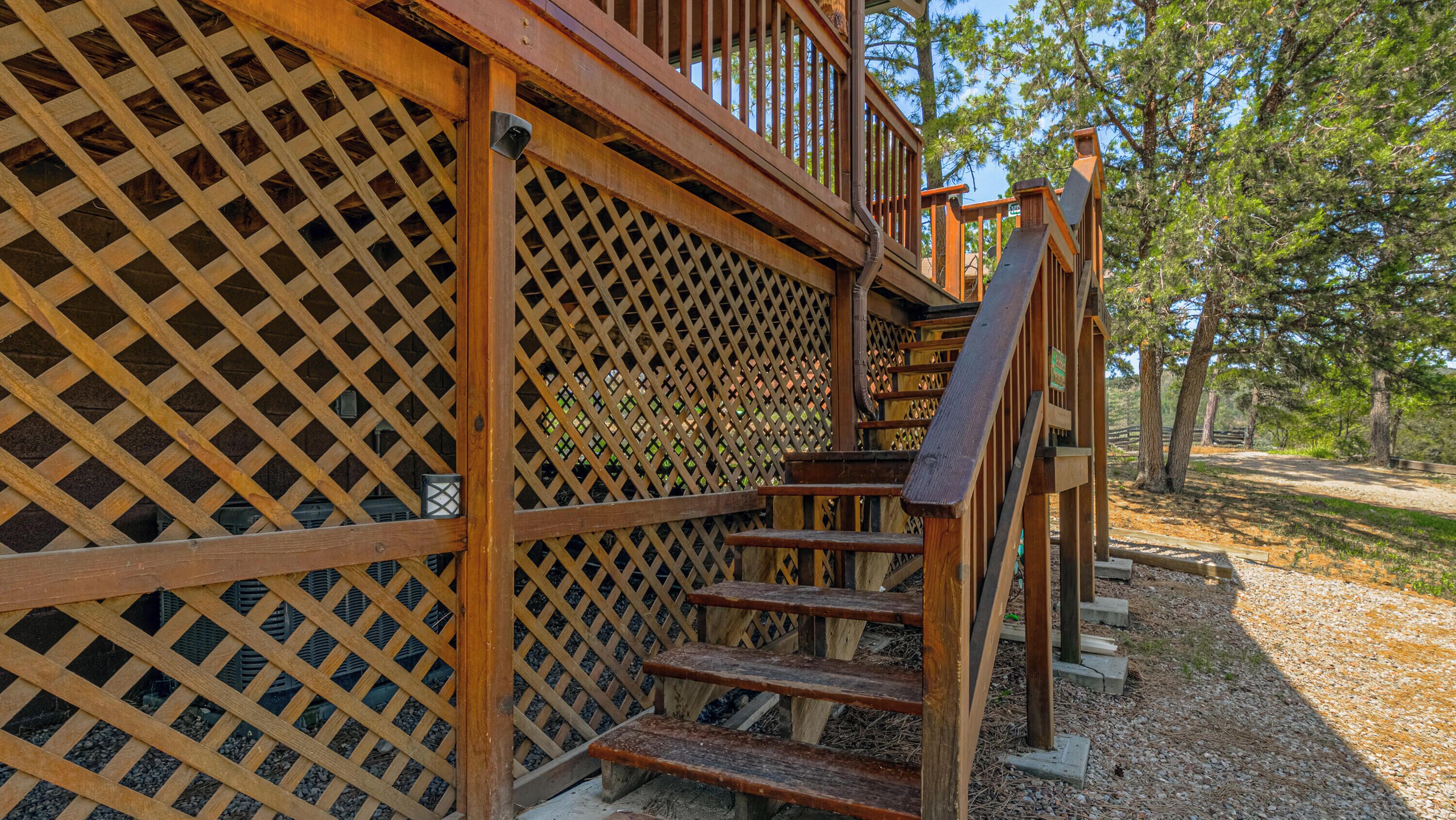 A wooden staircase leading to a covered area with a lattice design, surrounded by trees.