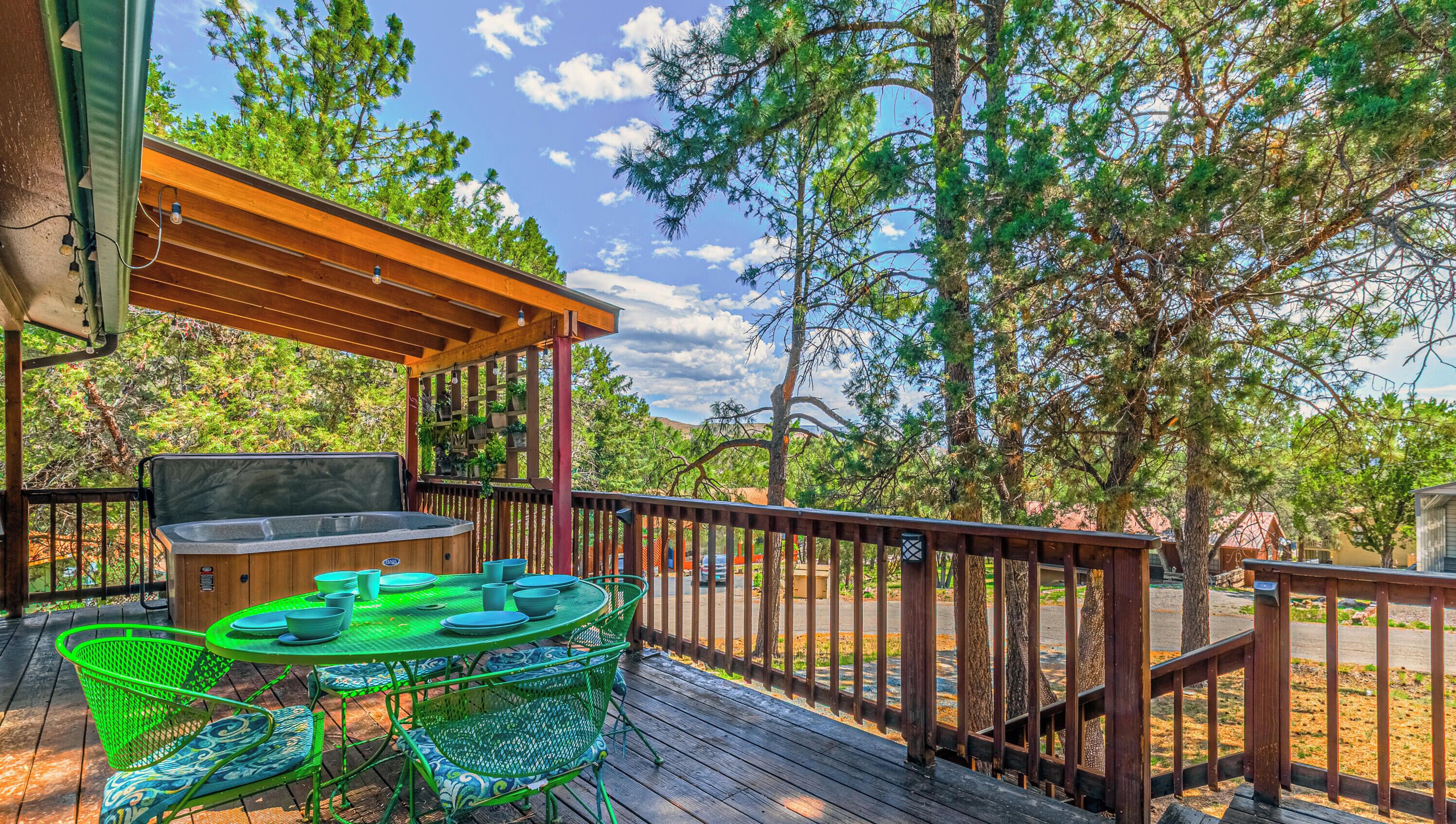 A wooden deck with a hot tub, outdoor table, and chairs, surrounded by trees.