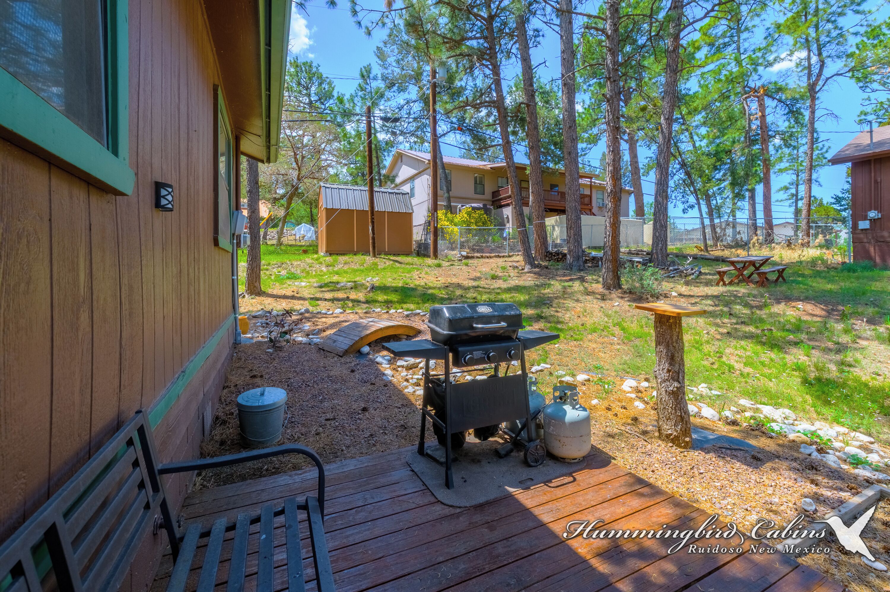 Eine Holzterrasse mit Grill, Picknicktisch und einer kleinen Gartenhütte.
