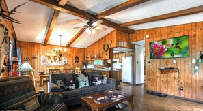 A rustic interior with wooden walls, a ceiling fan, a television, and a dining area. - Hidden Treasure | Strike Gold w/ Hot Tub Nights, Cozy Cabin Charm & Pet Friendly (Ruidoso)
