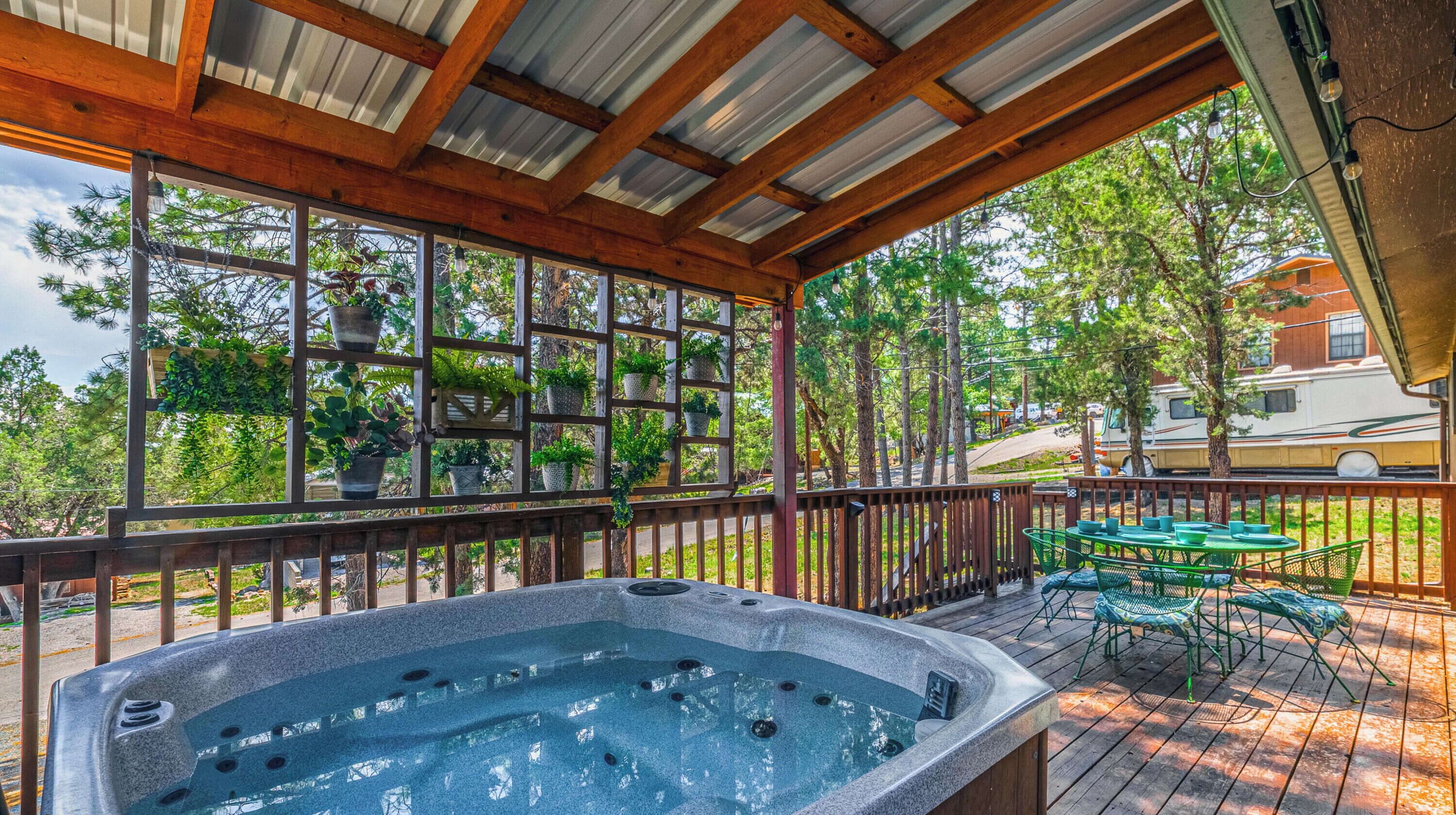 A hot tub under a wooden pergola with a view of trees and a parked RV.