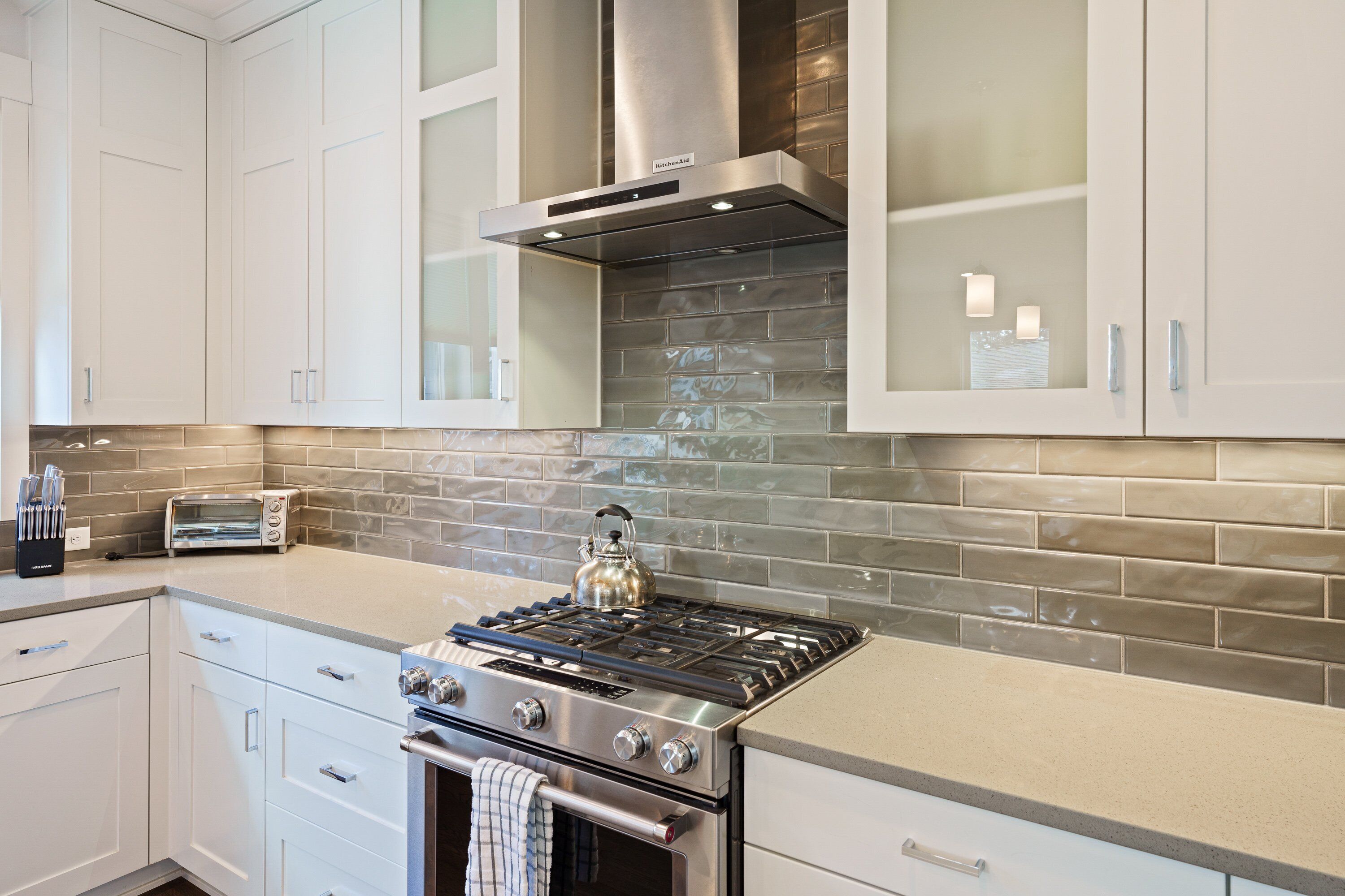 A modern kitchen with white cabinetry, a stainless steel range hood, a gas stove, and a tiled backsplash.