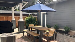 An outdoor patio with a wooden table and chairs, a blue umbrella, and a grill. - Hillside Haven - Bend's West Side, Work-from-Home Office, New, Modern, Light, Bright (Bend)