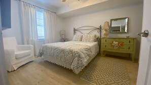 Une chambre à coucher comprenant un lit, une chaise, une table de chevet, une commode, un ventilateur de plafond et un tapis à motifs.