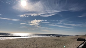 Une plage avec un ciel dégagé, un soleil éclatant et des vagues qui se rapprochent du rivage.