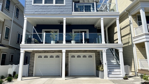 Un immeuble résidentiel de deux étages doté d’un balcon, de deux portes de garage et d’une façade en pierre.