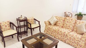 Una sala de estar con un sofá floral, dos sillas de madera, una mesita redonda y una mesa de centro de vidrio.