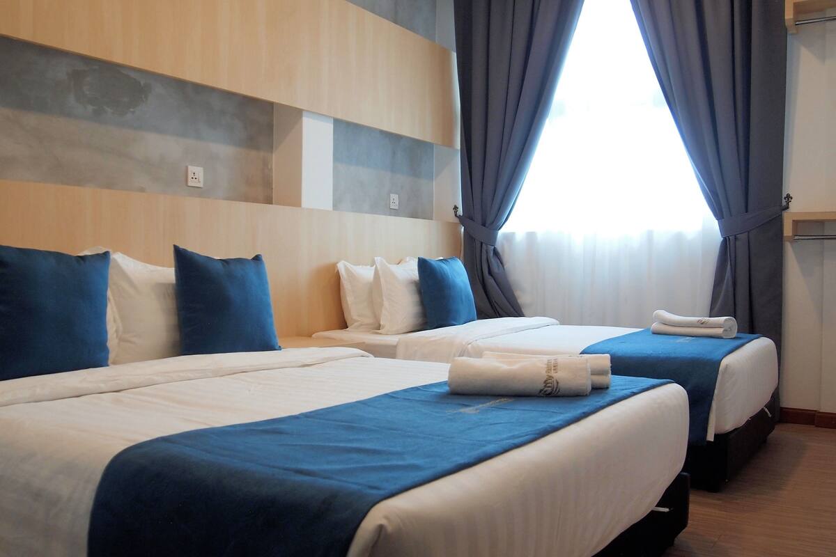 A hotel room with two beds, each with blue and white bedding, and a large window with curtains.