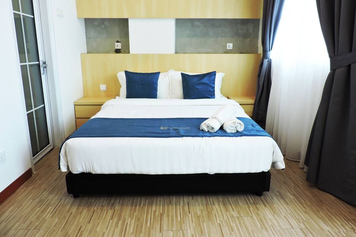 A hotel room with a bed, wooden floor, and a view of the outside.