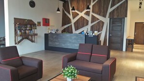 A reception area with a modern design, featuring a reception desk, two sofas, and a small table with a flower arrangement. - My Rainforest Suite Hotel (Langkawi)