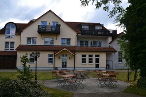 A two-story building with a balcony on the upper floor, a front entrance, and a patio area with tables and chairs.