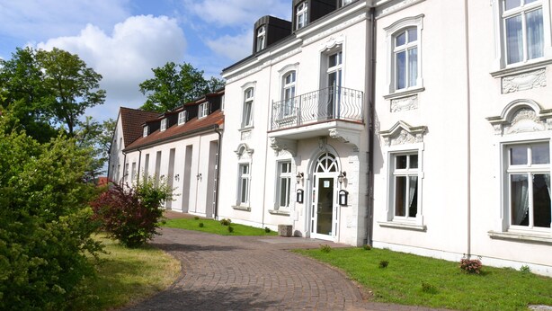 A traditional European building with a cobblestone driveway, large windows, and a well-maintained lawn.